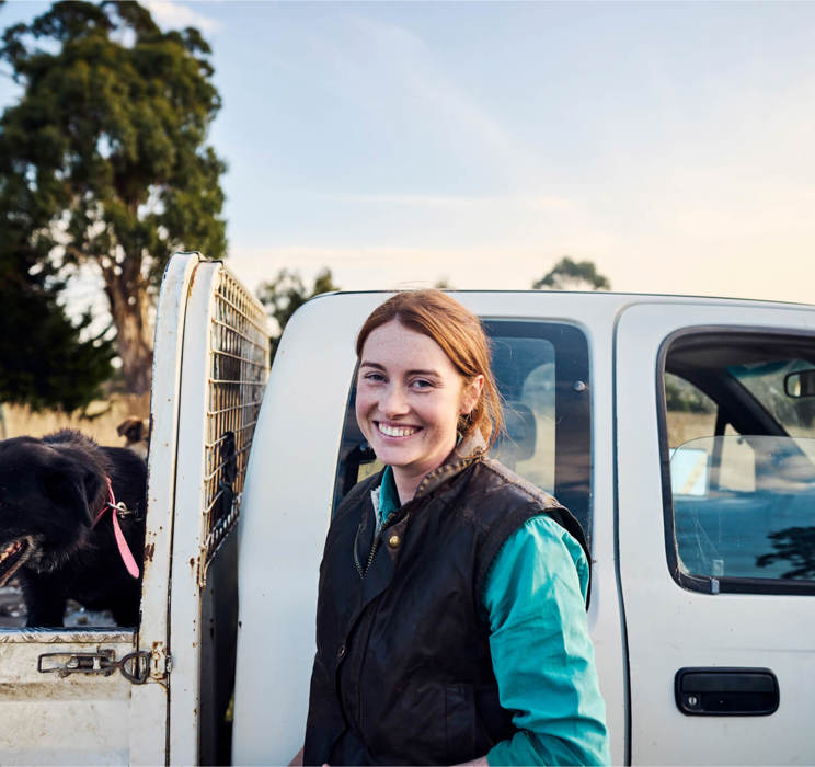 A farmer with her dog in the back of a ute